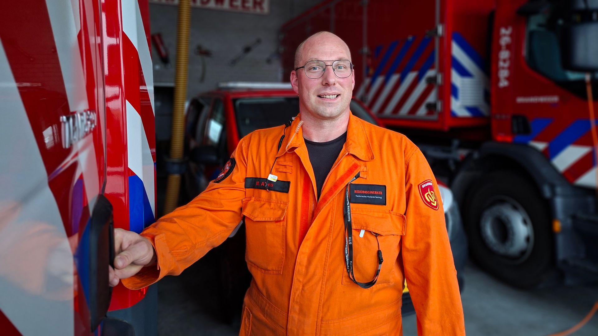 Marnix Abels staat in zijn oranje STH-uniform bij een brandweervoertuig.